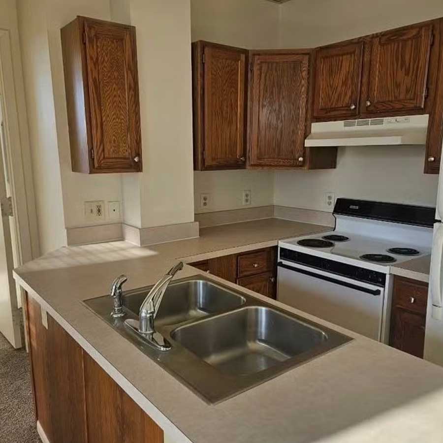 Cozy Hereford & Hops Delta Apartments kitchen with wood cabinets and a double sink.